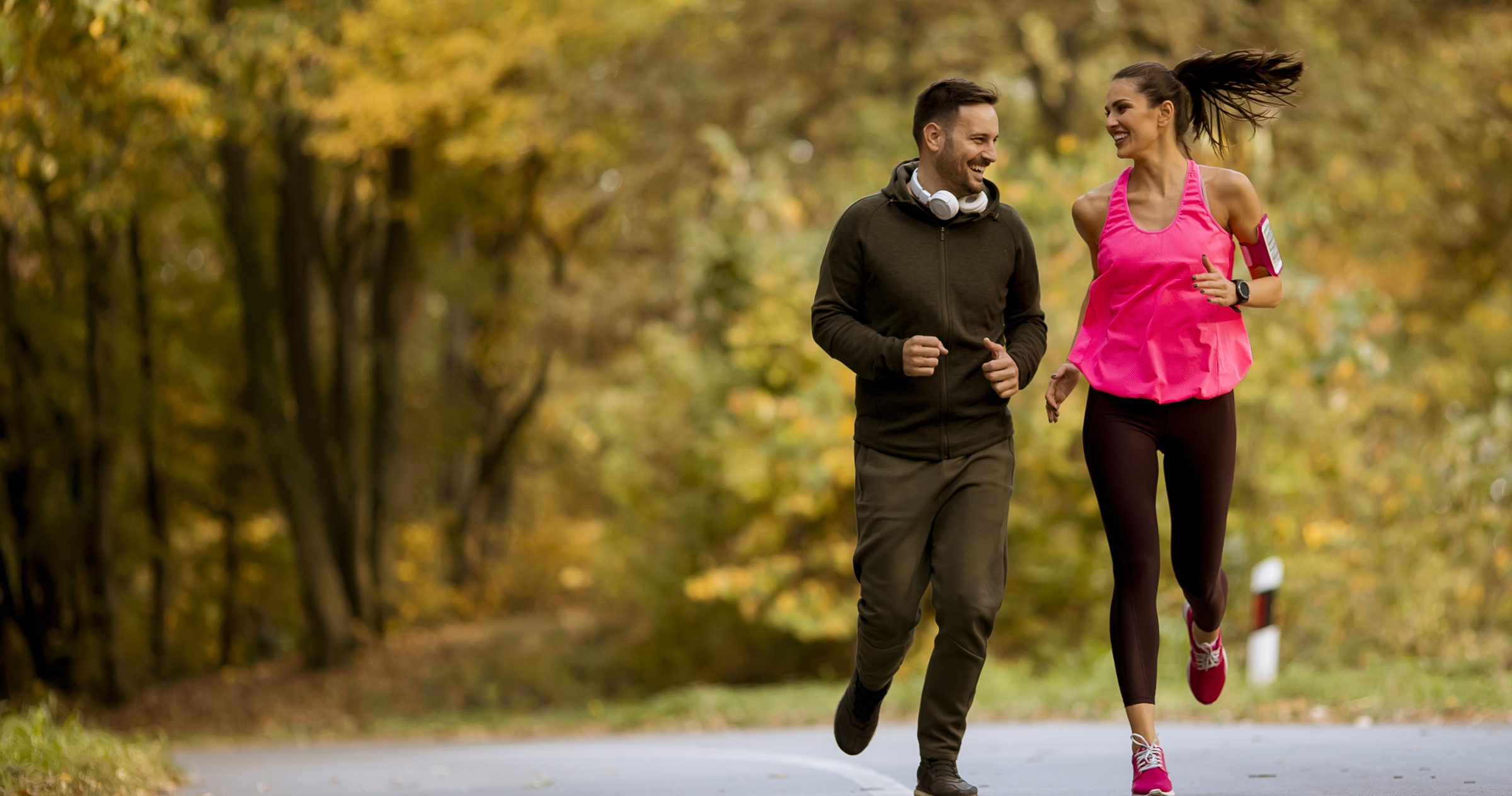 A woman and a man jogging side by side on a tree lined road in autumn